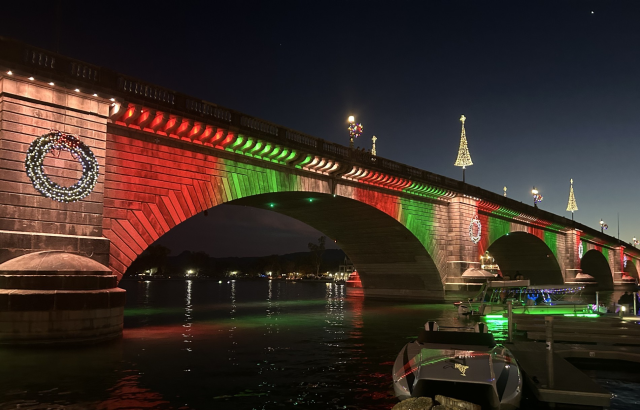 A stone bridge, at night, decorated with green and red holiday lights.