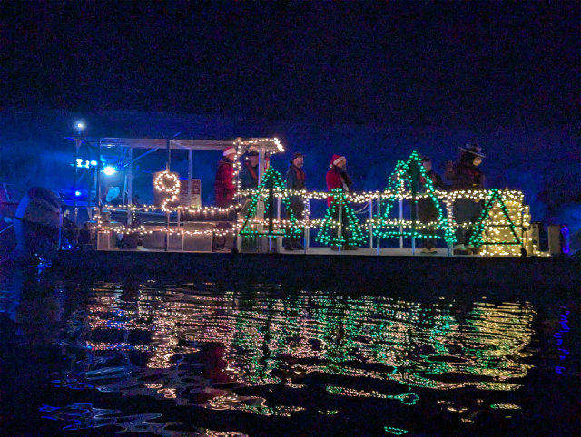 A boat, at night, decorated with holiday lights, with people dressed up in holiday costumes.