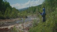 BLM staff stands to the side of a stream in waders taking stream measurements in the Steese NCA in interior Alaska.