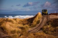 a 4x4 vehicle drives down a dirt path near the ocean