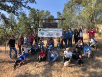 Group of volunteers sit on a dry grassy hill near a npld sign